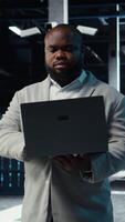 Vertical Data center admin coding, writing script on laptop, identifying bottlenecks. Server farm IT expert typing on notebook keyboard, troubleshooting bugs, implementing optimizations, camera A video