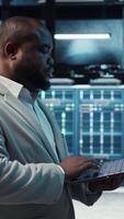 Vertical Manager overseeing server room, walking around with checklist on laptop, troubleshooting hardware. Supervisor doing inspection in server hub, overseeing infrastructure performance, camera A video