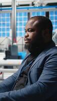 Vertical African american master engineer reviews operations in a solar tech plant, ensuring factory activity to meet green energy targets. Specialist uses tablet for manufacturing efficiency. Camera A. video