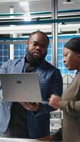 Vertical Black factory inspectors engaging in a briefing over the manufacturing process, reviewing production line and metrics on files. Supporting renewable energy improvement. Camera A. video