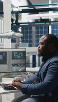 Vertical Black alternative energy consultant handling operations in a solar tech plant, ensuring factory practices meet green energy goals. Specialist uses pc for manufacturing efficiency. Camera A. video