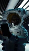 Vertical Astronaut researcher wearing equipment using tablet to carry out research. Scientist wearing cosmonaut gear in spaceship monitoring life support systems during flight using device, camera A video
