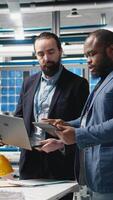 Vertical Diverse team of engineers and specialists collaborate in a solar panel factory, review blueprints and share ideas to enhance renewable energy production and sustainable innovation. Camera A. video