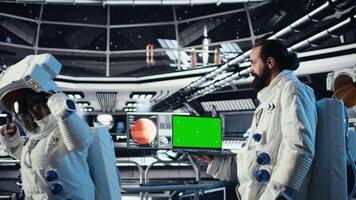 Team of astronauts checking human expansion in space mission logs on green screen laptop. Cosmonauts using chroma key notebook during mankind survival expedition, camera A video