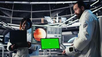 Astronaut monitoring system diagnostics on isolated screen tablet, chatting with colleague during space mission. Teamworking cosmonauts using mockup during cosmic expedition, camera A video