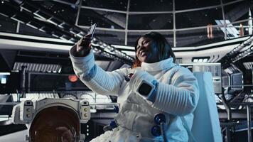 Jolly astronaut having fun in starship doing selfies using smartphone camera. Upbeat cosmonaut aboard space station doing photos on mobile phone during cosmic journey, camera A video
