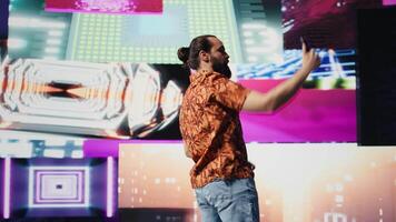 Cool relaxed guy using his smartphone under neon lights, capturing photos and videos as a content creator and DJ. Modern carefree person enjoys visual art in a nightlife scene. Camera B.