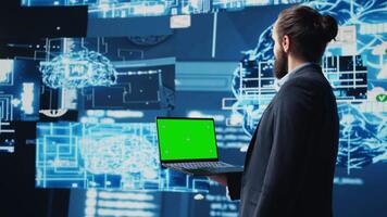 Business AI expert holding green screen on device next to brain animation, ensures implementing neural networks system. Young specialist analyzing algorithms and coding tools. Camera B. video