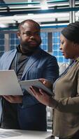 Vertical African american engineers team collaborating in a solar panel facility, examining blueprints to guarantee production line infrastructure and sharing ideas for alternative energy. Camera A. video