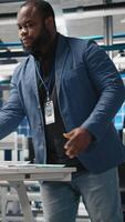 Vertical African american technician consulting performance metrics on papers and laptop, combining solar power expertise and efficiency in photovoltaics manufacturing industry. Camera A. video