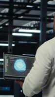 Vertical Technician using laptop in data center, managing server virtualization, running scripts. IT expert using programming language on notebook in server hub, finetuning network protocols, camera B video