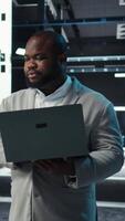 Vertical Data center engineer coding on laptop, doing software updates for mainframes. Server farm IT professional typing on notebook keyboard, optimizing infrastructure, camera A video
