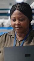 Vertical African american female expert reviewing solar panels production line, doing quality control in a photovoltaics factory. Analyzing data reports and insight to create solar power. Camera B. video