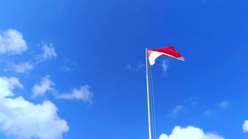 The Indonesian national flag flutters against a cloudy blue sky background from a low angle camera. The red and white flag. The Unitary State of the Republic of Indonesia video