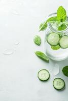 Refreshing Drink with Cucumber and Mint Leaves in Glass. Cold Beverage for Health and Fitness on White Surface. Water Drops Around Glass. photo
