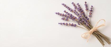 Lavender stems tied with string on a white surface. Purple flowers close up. Natural light. Small bouquet. Dried herbs arrangement. Simple flower bundle. photo