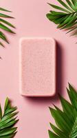 Pink soap bar lies flat on a pink surface. Green palm leaves are around it. The bar is centered and textured. photo