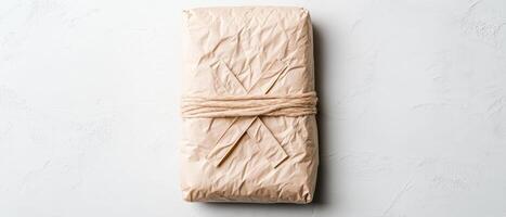 Wrapped package on a neutral surface. Brown paper held with simple twine. Rectangular form. Plain covering. Rustic wrapping. Minimalist aesthetic. Top view arrangement. photo