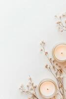 Burning candles in glass jars near small dried white flowers on a simple white surface providing quiet warmth and soft decorative accents photo