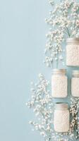 White flowers border containers with white beads on light blue textured surface. Minimal arrangement with simple decorations creates calm visual space. photo