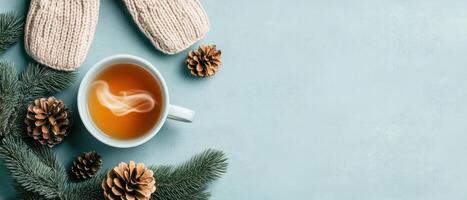Warm drink steams in cup with mittens fir branches and pine cones on blue background. Winter cozy scene with copy space. photo
