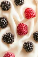 Fresh blackberries and raspberries scattered on a soft white fabric with delicate folds. Vivid red and deep black berries in natural light. photo