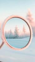 Snow covered trees reflection within circular mirror. Winter scene. Ice crystals form along the mirror edge. Cold icy field. Blue sky and pink light. photo
