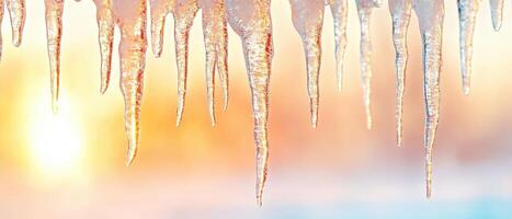 Frozen icicles hang against bright sunny sky. Melting ice drips during winter. Cold seasonal temperature create water formation. Close up of translucent crystal shape. photo