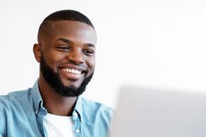 Closeup Shot Of Smiling Young Black Man Using Laptop. Positive African American Freelancer Guy Working On Laptop Computer, Looking At Screen With Pleased Face Expression, Enjoying Remote Job photo