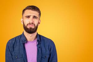 Young Caucasian man feeling unhappy, crying or whining on color studio background. Upset bearded guy with melancholic face expression having problem, suffering from stress or depression photo