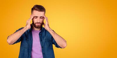 Young man suffering from headache, massaging his temples to ease pain on grey studio background. Millennial guy having high blood pressure, feeling stressed or tired, cannot solve problem photo
