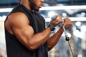 Concentrated black sportsman training muscles on block exerciser in gym, side view, copy space. Motivated african american bodybuilder having workout at modern gym, using peck deck machine photo