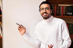 Knowledge And Education. Indian Male Teacher Teaching Online Pointing To Blackboard With English Language Grammar Rules Standing Indoor, Smiling To Camera. Distance Teaching And Learning Concept photo
