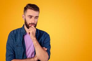 Dreamy young guy thinking over problem, touching his chin on grey studio background. Millennial hipster man making hard choice or decision, imagining something, having doubts photo
