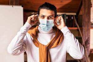 Quarantine. Indian Teacher Man Wearing Protective Face Mask Standing Near Blackboard With English Grammar Rules At Home. Distance Teaching And E-Learning, Online Remote Lectures, Classes And Lessons. photo