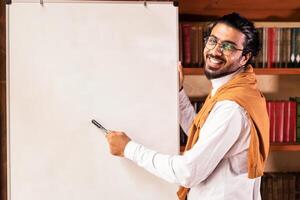 E-Teaching. Indian Teacher Man Posing Near Blackboard Having Online Class Of English Language Indoor, Smiling To Camera. Grammar Rules. E-Learning, Modern Education Concept photo