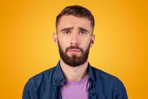 Millennial hipster guy feeling sad, lonely or depressed on grey studio background. Melancholic bearded man with unhappy face expression having trouble, suffering from stress or personal crisis photo