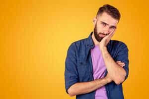 Portrait of bored Caucasian guy leaning on palm and looking at camera on orange studio background. Millennial man being sick and tired of something, annoyed or disappointed, having dull day photo