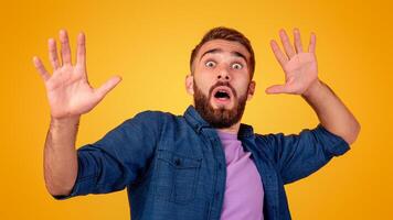 Scared Caucasian man making frightened gesture with his hands, trying to defend himself on orange studio background. Fearful young guy opening his mouth in shock, overwhelmed with emotions photo