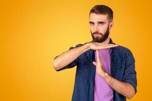Millennial bearded guy showing TIME OUT or STOP gesture over orange studio background. Young Caucasian man taking break or pause, running late, facing deadline, expressing rejection photo