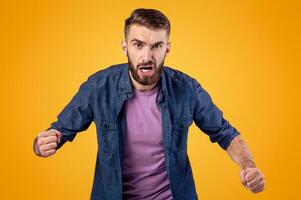 Portrait of young angry man shouting with rage, clenching fists on grey studio background. Furious Caucasian guy screaming with anger, expressing his frustration, ready for fight or conflict photo