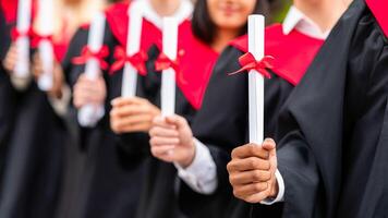 Hands of unrecognizable multiracial group of male and female graduators wearing graduation robes showing their diploma scrolls. High school, university college graduation concept photo