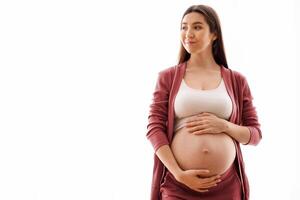 Young beautiful pregnant woman standing near window at home and touching belly, happy future mother tenderly embracing her naked tummy and looking away, enjoying pregnancy time, copy space photo
