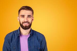 Carefree young guy looking at camera and smiling over orange studio background, panorama. Portrait of joyful bearded hipster man with happy face expression posing in casual outfit photo