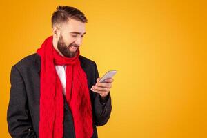 Happy businessman in formal suit and red scarf using smartphone, having online business call on orange studio background. Positive entrepreneur checking messages, reading news on cellphone photo