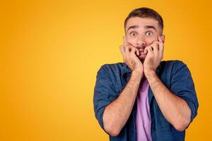Scared Caucasian guy biting his nails in terror over grey studio background. Young man feeling terrified, suffering from fear or shock, having panic attack. Expressing negative emotions concept photo
