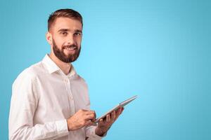 Funky millennial guy in formalwear using tablet computer for online work or studies on blue studio background, panorama with copy space. Young man communicating on internet, watching photo