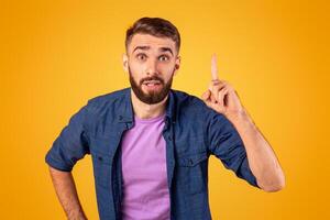Great idea. Young Caucasian guy pointing finger upwards, gesturing eureka, having inspirational AHA moment on orange studio background. Millennial man finding solution to complicated problem photo