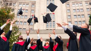 International group of students standing in a row and throwing graduation caps up in the air, posing next to university building after graduation ceremony, celebrating freedom photo