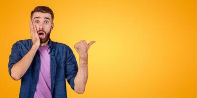 Promotion concept. Shocked hipster guy in casual outfit pointing aside at free space, recommending something, offering huge sale on orange studio background, banner design photo